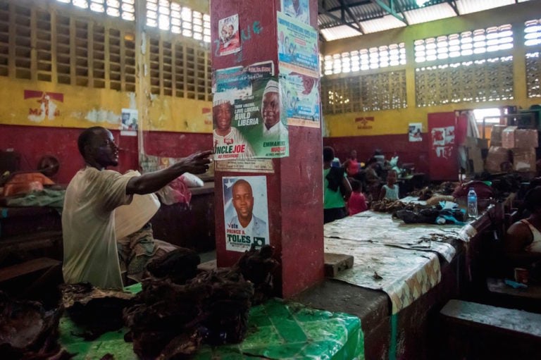 A man gestures by an electoral poster for candidates from the Unity Party, at a market in Monrovia, Liberia, 13 October 2017, CRISTINA ALDEHUELA/AFP via Getty Images