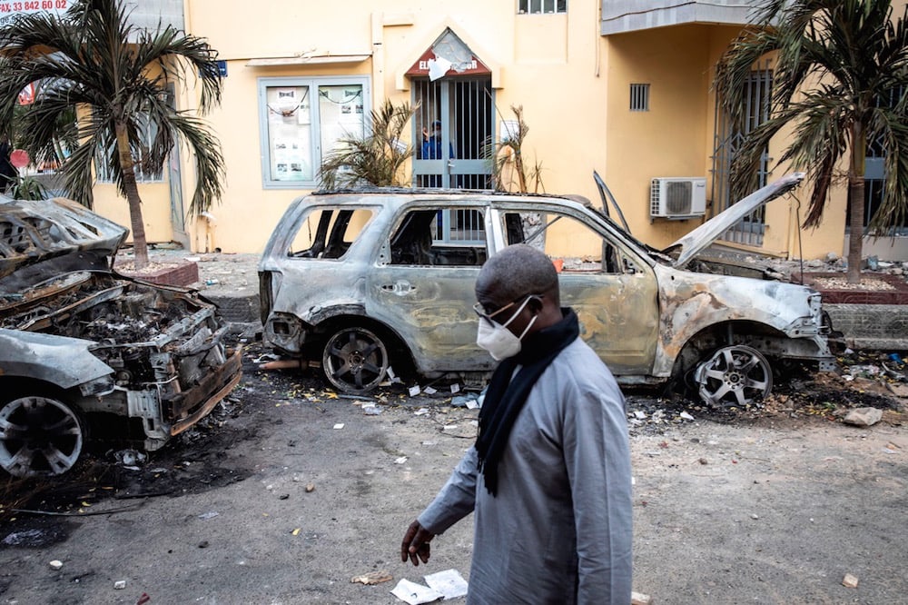 A man passes by the remains of two burned cars reportedly belonging to Radio Futures Media (RFM), after protesters targeted stations believed to be close to the government, Dakar, Senegal, 5 March 2021, JOHN WESSELS/AFP via Getty Images