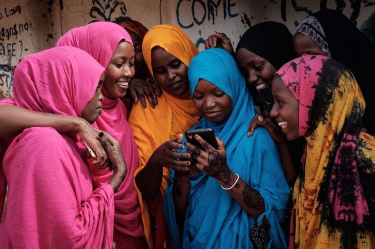 Young Somali refugee women look at a smartphone as they huddle together at the Dadaab refugee camp, in the north-east of Kenya, 16 April 2018, YASUYOSHI CHIBA/AFP via Getty Images