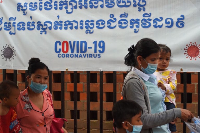 Women wearing face masks to reduce the spread of COVID-19 walk with their children past a hospital banner warning about the virus, Phnom Penh, Cambodia, 29 September 2020, TANG CHHIN SOTHY/AFP via Getty Images