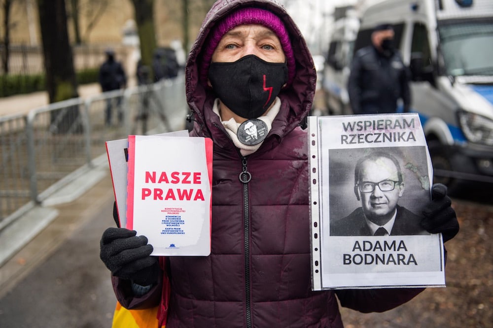 A supporter of Adam Bodnar holds a portrait of the Ombudsman and a book titled 'Our Rights', outside the Constitutional Tribunal, Warsaw, Poland, 15 April 2021, Attila Husejnow/SOPA Images/LightRocket via Getty Images