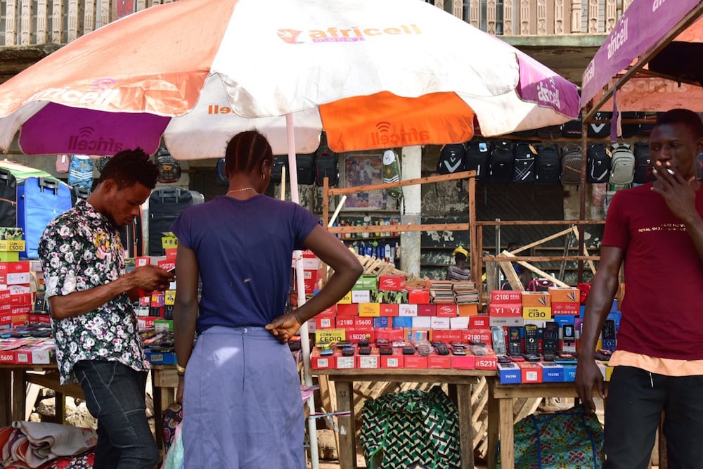 A mobile phone vendor helps a customer at a stall in the market in Makeni, northern Sierra Leone, 5 March 2018, ISSOUF SANOGO/AFP via Getty Images