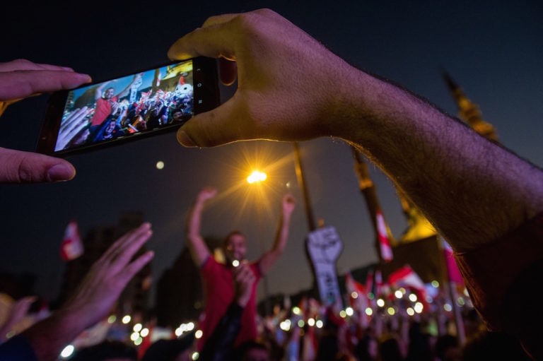 A man takes a video on his mobile phone as thousands of protesters rally beneath a sign of a large fist and the Arabic word for "Revolution", in Beirut, Lebanon, 3 November 2019, Scott Peterson/Getty Images