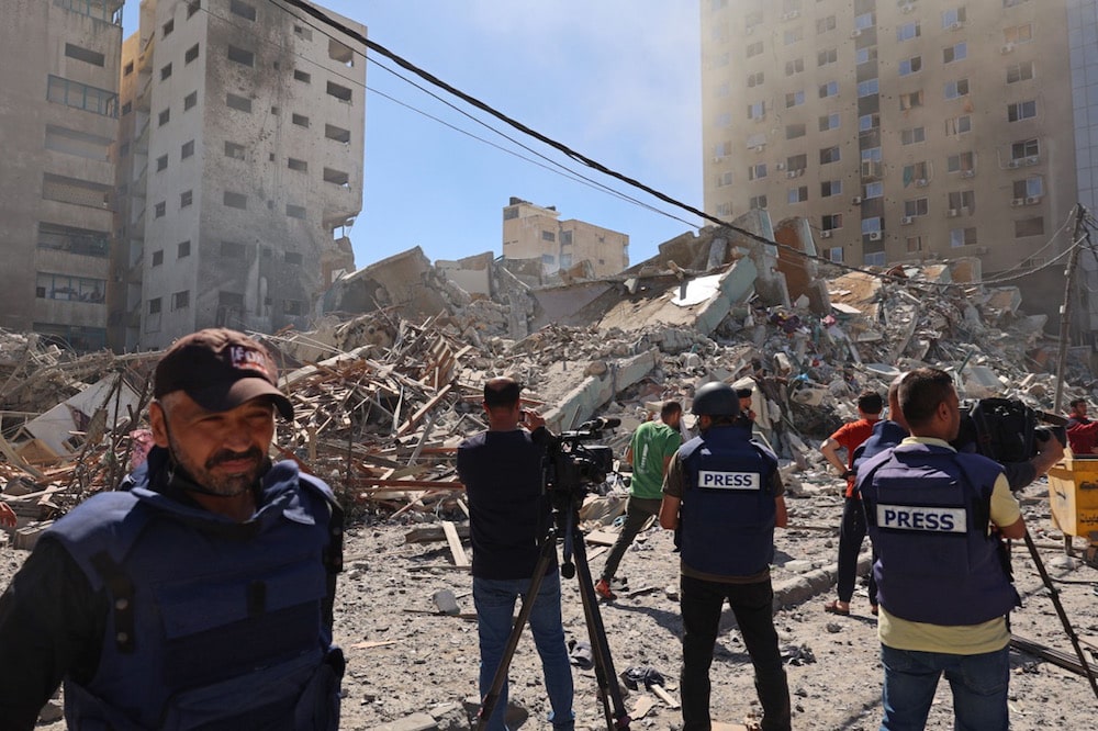 صحفيون فلسطينيون يغطون قصف برج الجلاء، الذي كان يضم عددًا من المكاتب الصحفية الدولية، والذي دمرته غارة جوية إسرائيلية، قطاع غزة، 15 أيار 2021. (الصورة من: محمد عابد / الوكالة الفرنسية عبر Getty Images).