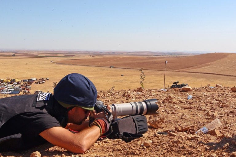 مصور صحفي على الأرض بينما يشتبك مسلحو داعش مع الجماعات المسلحة الكردية، في منطقة زورافا السورية، بالقرب من الحدود التركية، بتاريخ 1 تشرين الاول 2014. (الصورة من: أمين مينجوارسلان / وكالة الأناضول عبر Getty Images).