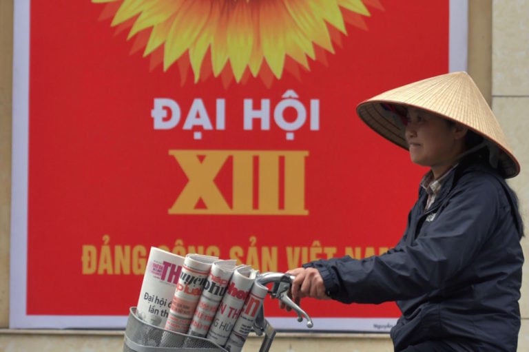 Une vendeuse de journaux va à vélo devant un panneau pour le congrès du Parti communiste vietnamien (PCV), Hanoi, le 26 janvier 2021, NHAC NGUYEN/AFP via Getty Images