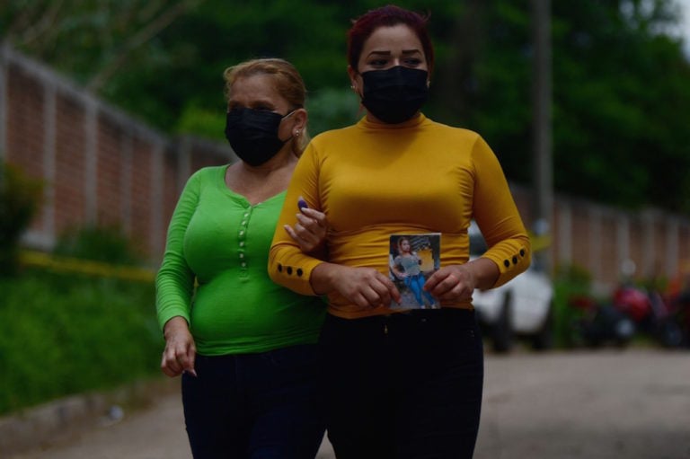 Familiares de una de las personas desaparecidas con una foto de ella, cerca de la vivienda de un expolicía donde agentes policiales realizan excavaciones en una fosa clandestina, Chalchuapa, El Salvador, el 27 de mayo de 2021, STR/AFP via Getty Images