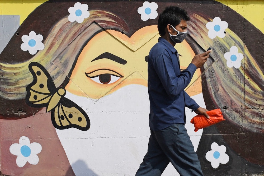 A man wearing a face mask as a precaution against the spread of COVID-19 uses his mobile phone as he walks past a mural, in Maharashtra, India, 21 January 2021, Ashish Vaishnav/SOPA Images/LightRocket via Getty Images