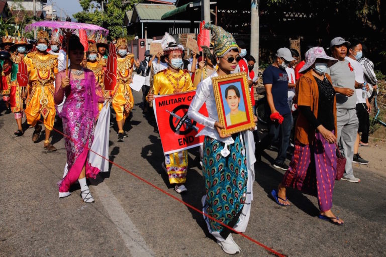 Protesters hold up an image of Aung San Suu Kyi and signs as they demonstrate against the military coup in Myeik, Myanmar, 12 February 2021, STR/AFP via Getty Images