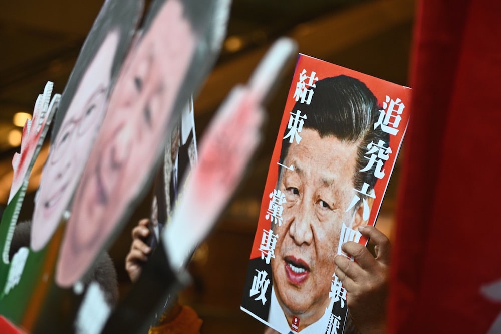 Pro-democracy activists display placards of Chinese President Xi Jinping and Hong Kong Chief Executive Carrie Lam, before boarding a ferry from Hong Kong to Macau during a visit by Jinping, 18 December 2019, PHILIP FONG/AFP via Getty Images