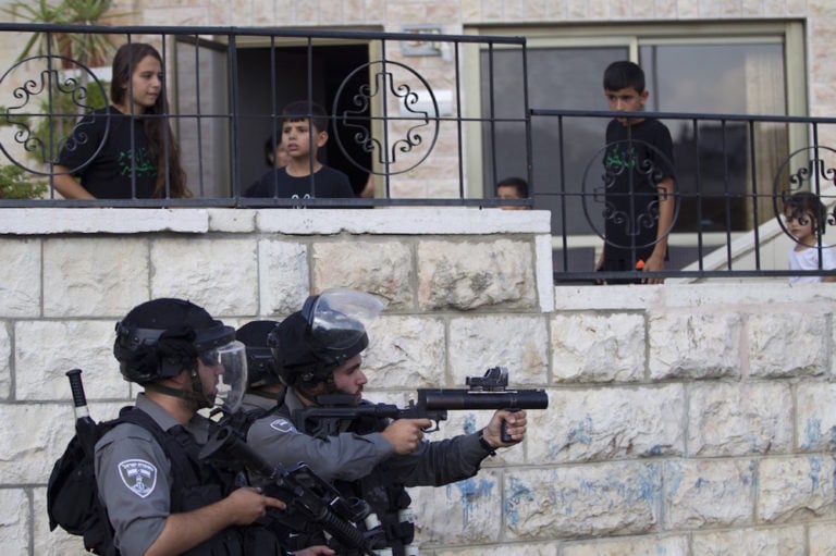 Palestinian youth look on as an Israeli police officer aims his weapon during a protest against the death of a Palestinian teenager, in the neighbourhood of Wadi Joz, East Jerusalem, 7 September 2014, AHMAD GHARABLI/AFP via Getty Images