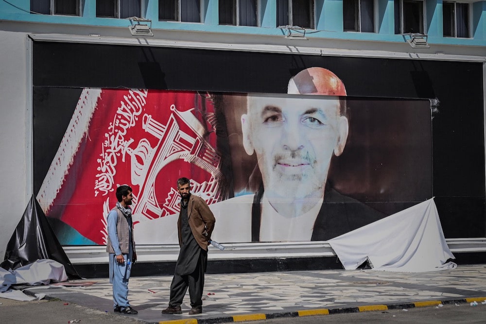 Two men stand next to a torn poster of Afghan President Ashraf Ghani at the Kabul airport, in Kabul, 16 August 2021, as thousands of people headed to the airport to try to flee, WAKIL KOHSAR/AFP via Getty Images