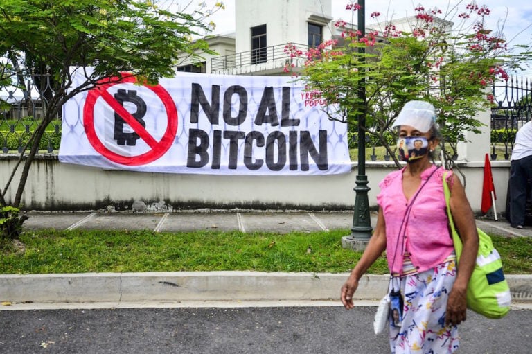 Una mujer pasa en frente de una banderola durante una protesta contra la nueva ley que regula la criptomoneda Bitcoin, en San Salvador, El Salvador, el 20 de julio de 2021, Camilo Freedman/SOPA Images/LightRocket via Getty Images