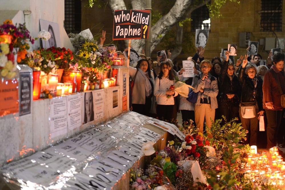 People hold portraits as they stand beside a memorial created in memory of murdered journalist Daphne Caruana Galizia, on the six-month anniversary of her death, outside the law courts in Valletta, Malta, 16 April 2018, MATTHEW MIRABELLI/AFP via Getty Images