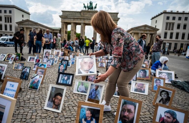 A protester places portraits of Syrians suspected of being detained or disappeared by the Syrian government on the pavement during a demonstration in front of Berlin's Brandenburg gate on 7 May 2022. JOHN MACDOUGALL/AFP via Getty Images